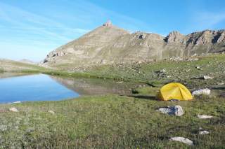 Trekking-Zelt neben einem Bergsee in karger Gebirgslandschaft