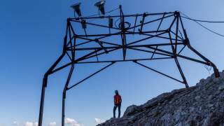 Bergsteigerin steht unter einem Stahlgerüst aus der Zeit des Baus der Zugspitzbahn.