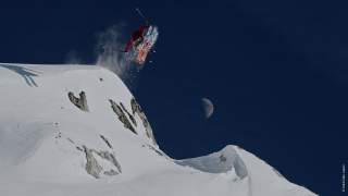 Skifahrerin springt von einer schneebedeckten Felskante vor dunklem Himmel mit sichtbarem Halbmond ab.