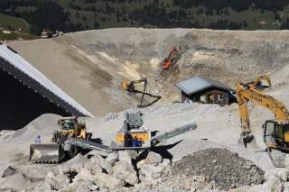 Bagger in einer großen Mulde am Ausbaggern eines Speicherteichs für künstliche Beschneidung.