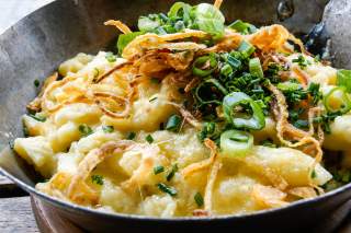 Käsespätzle mit knusprigen Röstzwiebeln und gehacktem Schnittlauch in einer Pfanne serviert.