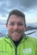 lächelnder Mann in grüner Jacke in den Bergen