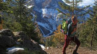 Wanderin läuft Bergweg hinauf, im Hintergrund teils verschneite Berge