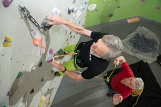 Mann klettert an Wand in Kletterhalle, anderer Mann sichert