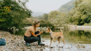 Frau und Hund spielen an Flussufer