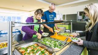 Drei Menschen stehen um Salatbüffet und bedienen sich