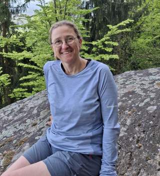 Lächelnde Frau mit Brille. Sie sitzt auf einem Stein