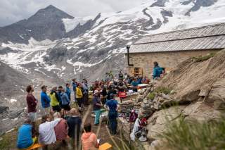 Eine Menschengruppe in Wanderkleidung vor der restaurierten Alten Prager Hütte. Im Hintergrund ein Gletscher (der Schlatenkees).