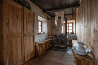 Historische Ausstattung der Alten Prager Hütte. Ein einfach eingerichteter Hüttenraum. Über einem gusseisernen Ofen hängt eine weiße, lange Wollunterhose.