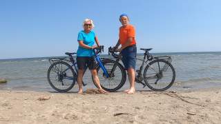 Paar steht mit Gravelbikes am Strand am Meer