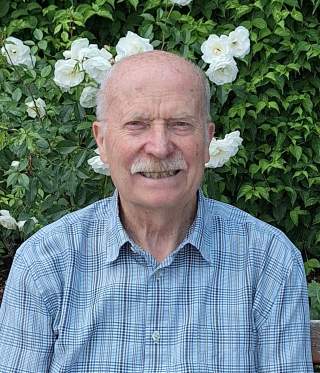 lächelnder Mann im karierten Hemd vor Hecke