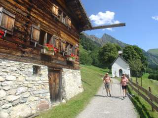 Zwei Menschen wandern an altem Bauernhaus vorbei