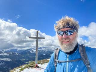 Mann neben Gipfelkreuz
