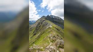 Person wandert auf Berggrat, der sich durchs Bild zieht