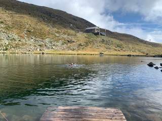 Mensch badet im Bergsee, Hütte im Hintergrund