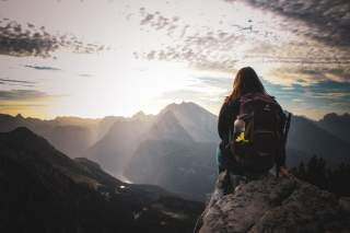 Frau sitzt auf Fels und genießt Aussicht auf Berge und See