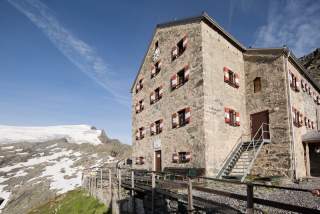 Eine mehrstöckige Alpenvereinshütte, gemauert aus Naturstein.