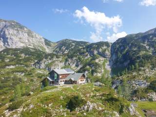 Auf einem Fels steht eine Hütte, ringsum kesselartig von Bergen umgeben.