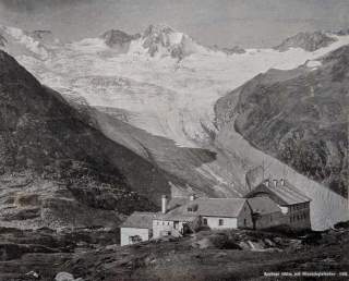 Ein Schwarzweißfoto aus dem frühen 20. Jahrhundert: Vor einem mächtigen Gletscher, dem Waxegg-Kees, steht die Berliner Hütte.