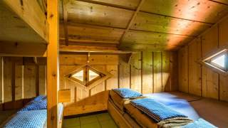 Ein holzvertäfelter Schlafraum auf einer Hütte mit Doppelstockbett und Matratzenlager.