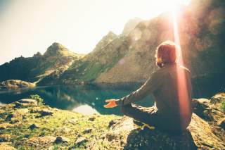 Mann sitzt an Bergsee und meditiert