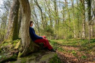 Frau sitzt in Wald an Baumstamm gelehnt