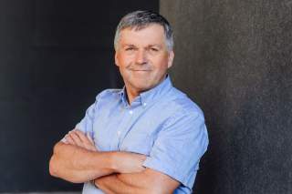 lächelnder Mann mit verschränkten Armen in blauem Hemd