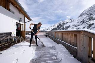 Frau schippt Schnee auf Hüttenterrasse