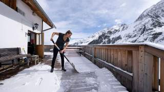 Frau schippt Schnee auf Hüttenterrasse