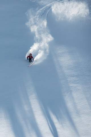 Ein Freerider fährt einen großen Schwung im frischen, bis dahin unberührten Schnee, der aufstaubt.