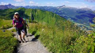 Frau wandert Bergweg hinauf, im Hintergrund Ausblick auf Bergketten