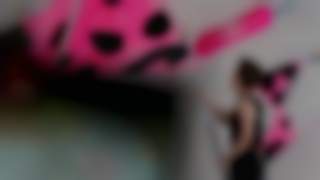 Ein Mann reinigt mit einem langen Werkzeug bunte, pink-schwarze Klettergriffe an einer Kletterwand.