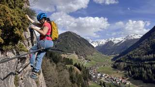 Eine Frau in einem Klettersteig. Im Hintergrund der Talboden und schneebedeckte Berge.