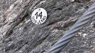 Metallplakette mit der Zahl 14 und der Aufschrift "SOS 140" an einer Felswand, davor ein Drahtseil.
