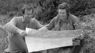 Josef Klenner und Begleitung halten eine Wanderkarte. Ein altes Schwarz-Weiß-Foto zeigt zwei junge Männer in Wanderkleidung. Sie sitzen auf dem Boden und blicken lachend in eine Wanderkarte.
