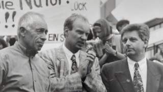 Schwarz-Weiß-Bild zeigt Heiner Geißler, Thomas Urban, Josef Klenner bei einer Demo 1994 in Stuttgart. Im Hintergrund sind Teile von Bannern zu sehen, die Schrift ist abgeschnitten, lesbar ist "Natur!"