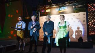 Siegerehrung Boulder Weltcup 2016. Auf einer Bühne stehen vier Personen, zwei von ihnen in bayerischer Tracht. Im Hintergrund ist eine Rückwand mit Logos zu sehen, links im Hintergrund eine Boulderwand mit roten Griffen.