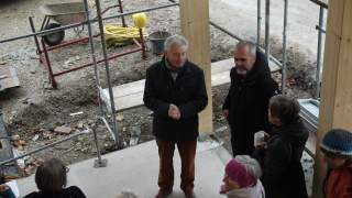 Josef Klenner und Architekt beim Richtfest. Das Foto zeigt einige Personen aus der Vogelperspektive auf einer Baustelle. Sie stehen auf Betonboden, an dessen Ecken sind Holzsäulen zu sehen, Wände gibt es noch nicht.