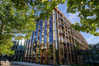 Die Bundesgeschäftsstelle des DAV in München-Schwabing. Durch grüne Blätter hindurch sieht man ein fünfstöckiges Gebäude aus Holz und Glas, eine Seite der Fassade ist bepflanzt.