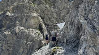 Zwei Menschen wandern in felsiger, mit Drahtseil gesicherter Berglandschaft