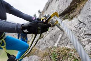 Mensch hängt Karabiner am Klettersteig ein