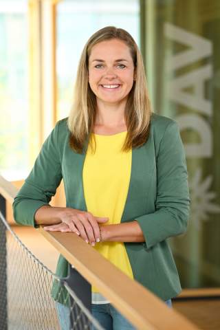 Sophie Hufnagl Sophie Hufnagl ist Referentin im Marketing Team des deutschen Alpenvereins. Sie trägt eine grüne Jacke, ein gelbes T-Shirt und lächelt. Sie steht im Treppenhaus der Bundesgeschäftsstelle. Das DAV Logo ist im Hintergrund.