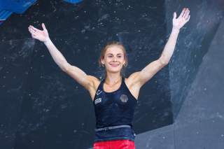 Hannah Meul steht vor einer Boulderwand und hebt die Hände wie eine Siegerin