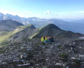 Rucksack liegt auf felsigem Untergrund, im Hintergrund Bergketten