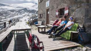 Drei Menschen sitzen in der Sonne auf Hüttenterrasse