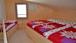 Ein helles, holzvertäfeltes Mehrbettzimmer auf einer Alpenvereinshütte.