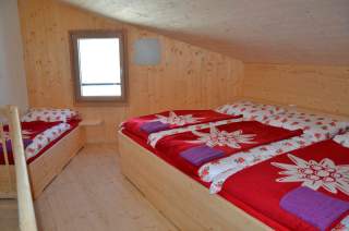 Ein helles, holzvertäfeltes Mehrbettzimmer auf einer Alpenvereinshütte.