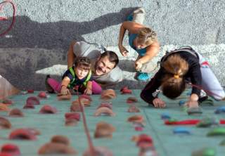 Familie klettert mit kleinem Kind draußen an Kletterwand