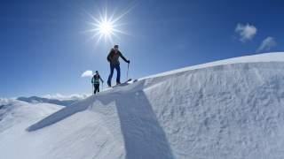 Frau und Mann steigen mit Ski auf einen Gipfel