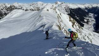 Mann und Frau auf Tourenski fahren von einem Gipfel ab